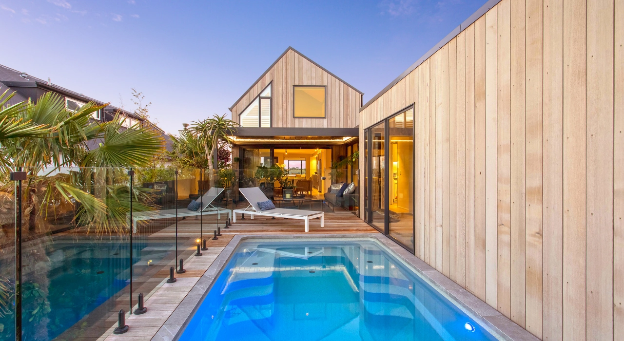 <img alt="Pool and cedar deck, asymmetrical roofline reflected in still water with warm interior light beyond." src="/images/d/o/n/-/r/don-roy-site-architecture-moncks-bay-chch-pool-yard-c2e15be6.webp?description" width="2560" height="1707" />