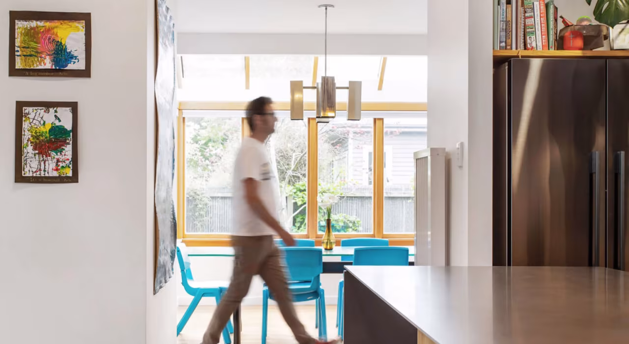 <img alt="Open-plan dining area with timber-framed windows, blue chairs and a figure walking through the sunlit space." src="/images/s/i/t/e/-/site-arch-grange4-00134059.webp" width="2560" height="1705" />