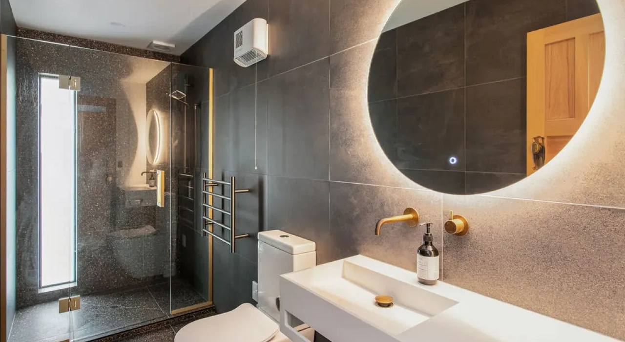 <img alt="Dark tiled bathroom with large circular backlit mirror, warm timber vanity and textured wall tiles." src="/images/s/i/t/e/-/site-arch-grange7-b589cb06.webp?description" width="1024" height="683" />