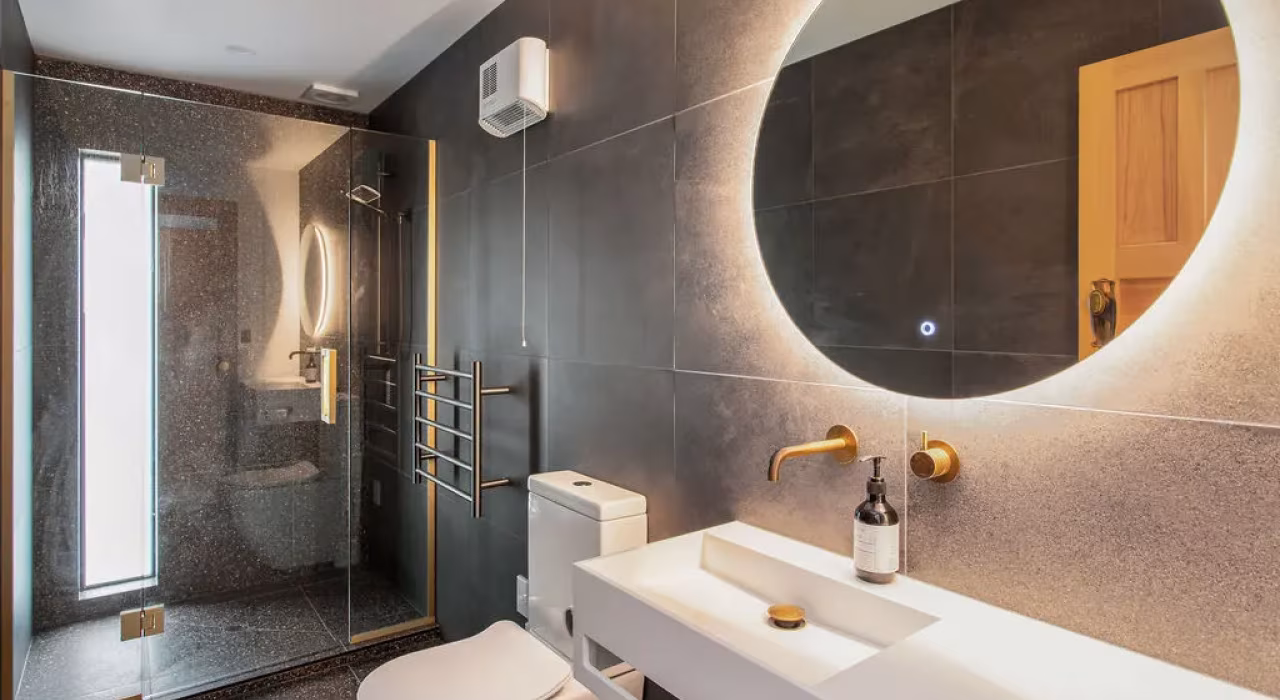 <img alt="Dark tiled bathroom with large circular backlit mirror, warm timber vanity and textured wall tiles." src="/images/s/i/t/e/-/site-arch-grange7-377668f4.webp" width="1024" height="683" />