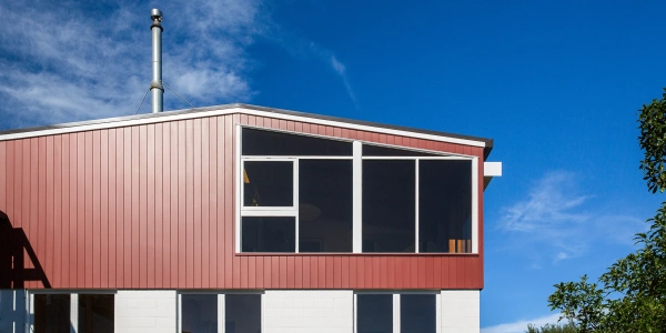 Exterior of Hillside Modern renovation, red coloursteel cladding and mid-century roofline under a wide blue sky, Christchurch.