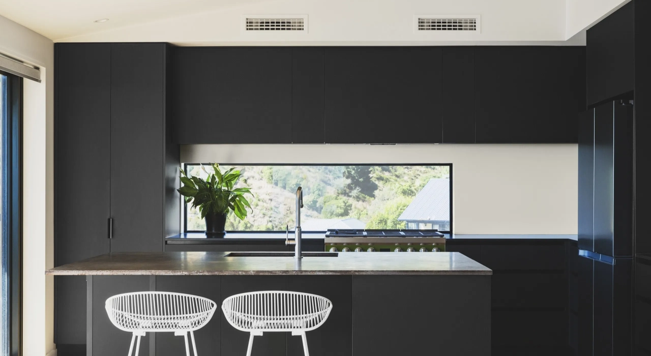 <img alt="Dark kitchen with island bench, white stools and a window framing the landscape outside." src="/images/s/i/t/e/-/site-architecture-drayton-drive11-cc1c9515.webp?description" width="2560" height="1706" />